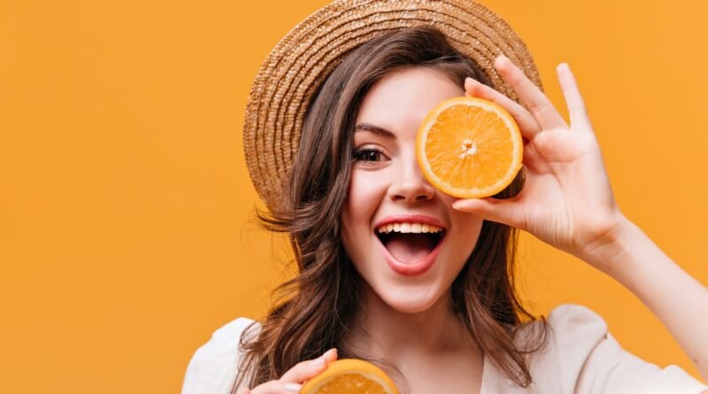 Frutas com vitamina C: na imagem uma mulher sorridente segura uma laranja partida em frente ao olho.
