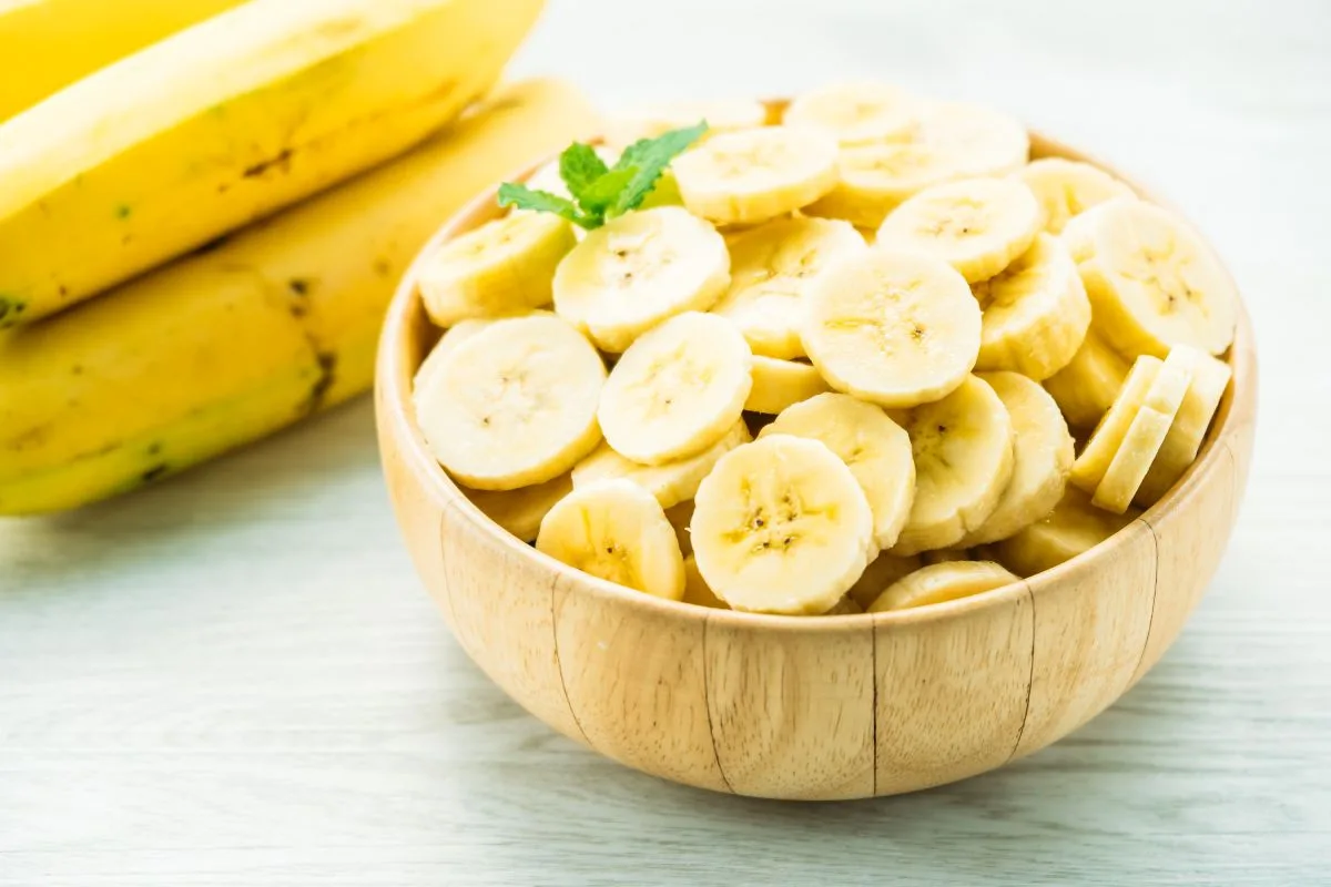 Banana: veja seus benefícios, calorias e como consumir 1 fatias de banana amarela crua na tigela de madeira